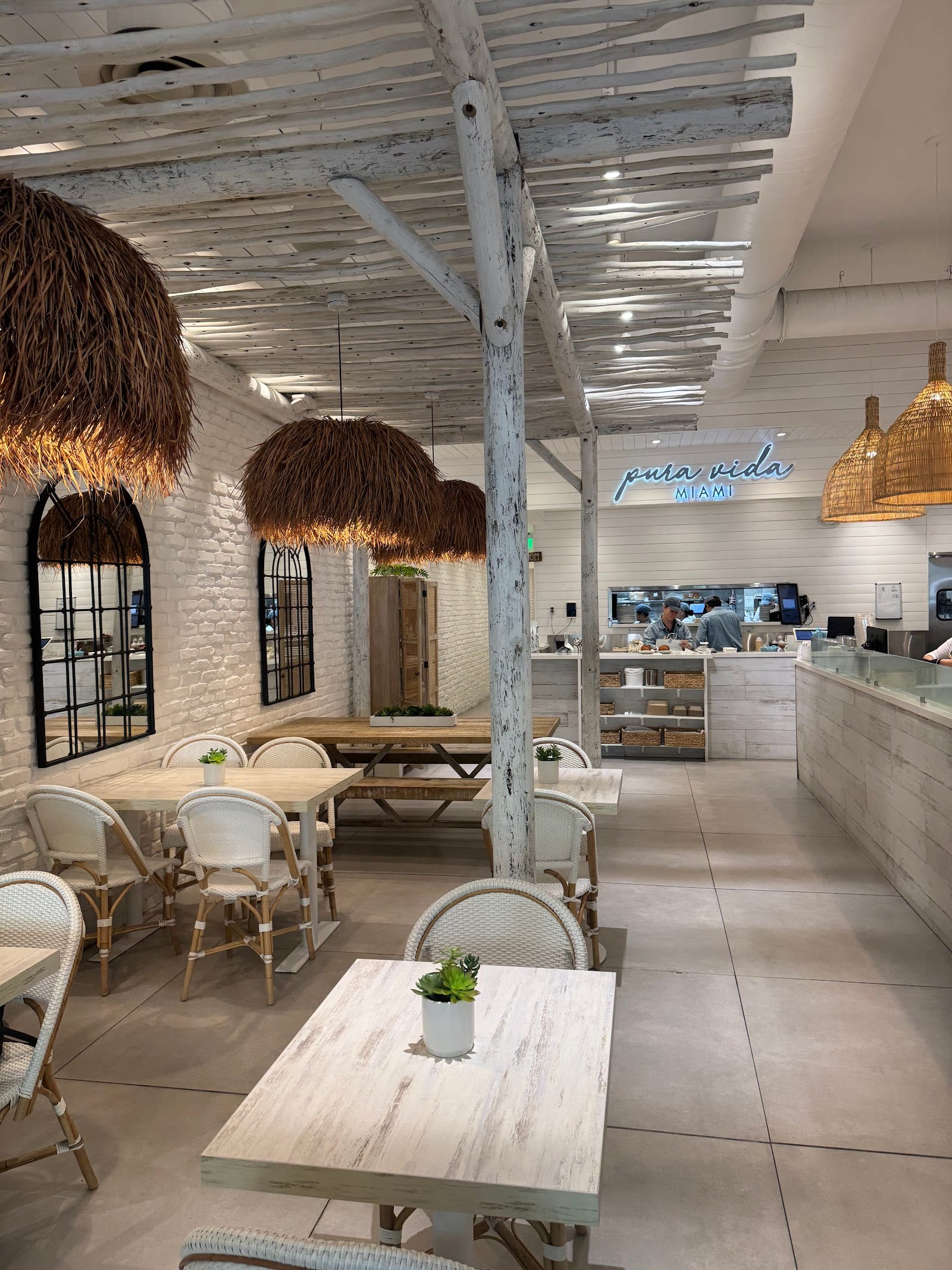 The bright dining room at Pura Vida on Miracle Mile in Coral Gables, with a large communal table and the order counter behind it