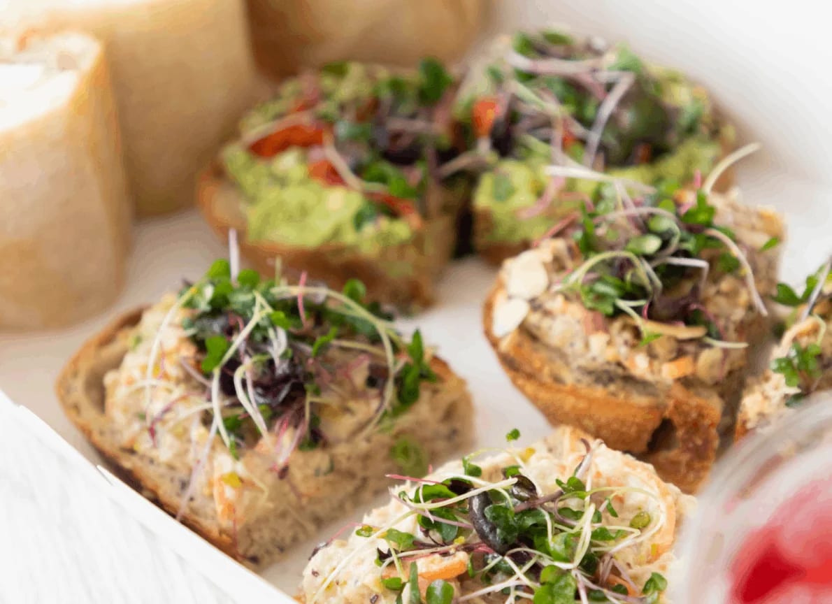 GROU catering platter of avocado, tuna and garbanzo toasts topped with microgreens beside panini rolls