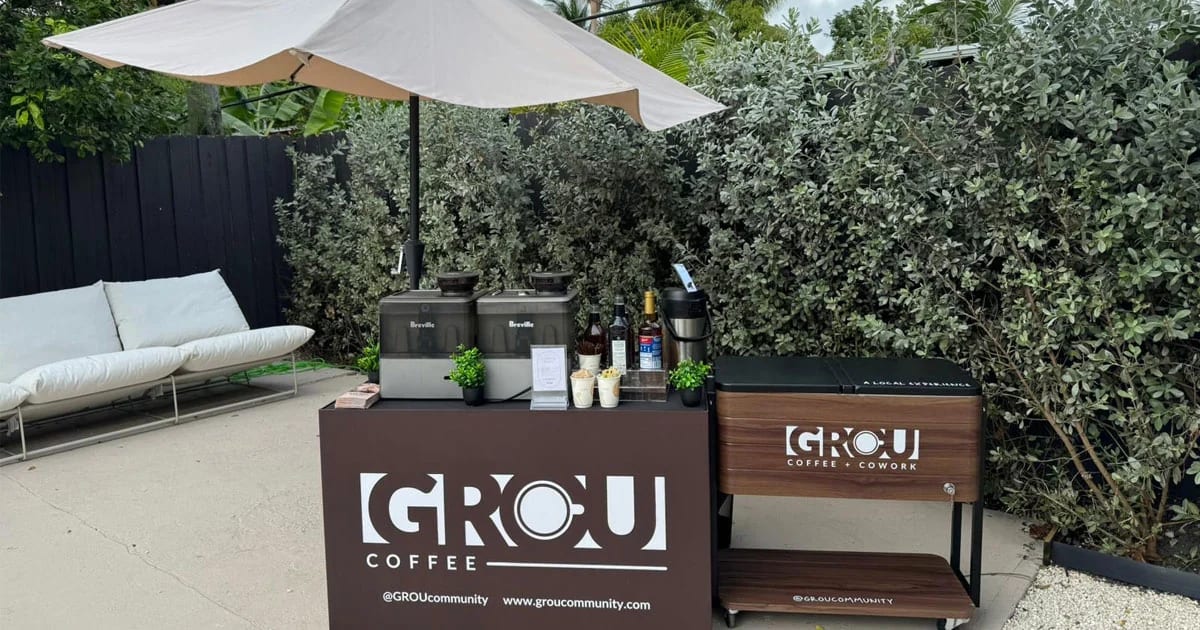 The GROU branded coffee cart set up outdoors with two brewers, syrups and cups under a patio umbrella